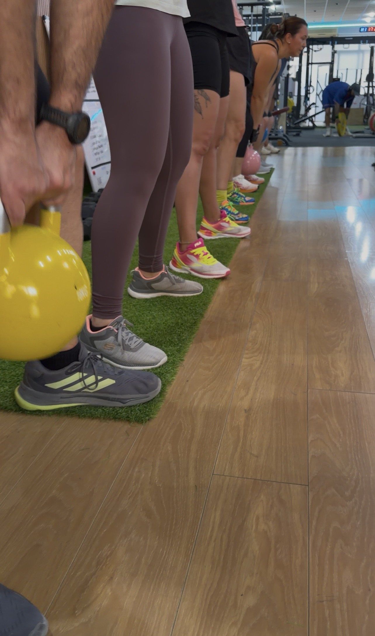 Kettlebell amarilla en el suelo con el grupo en fila sobre el césped