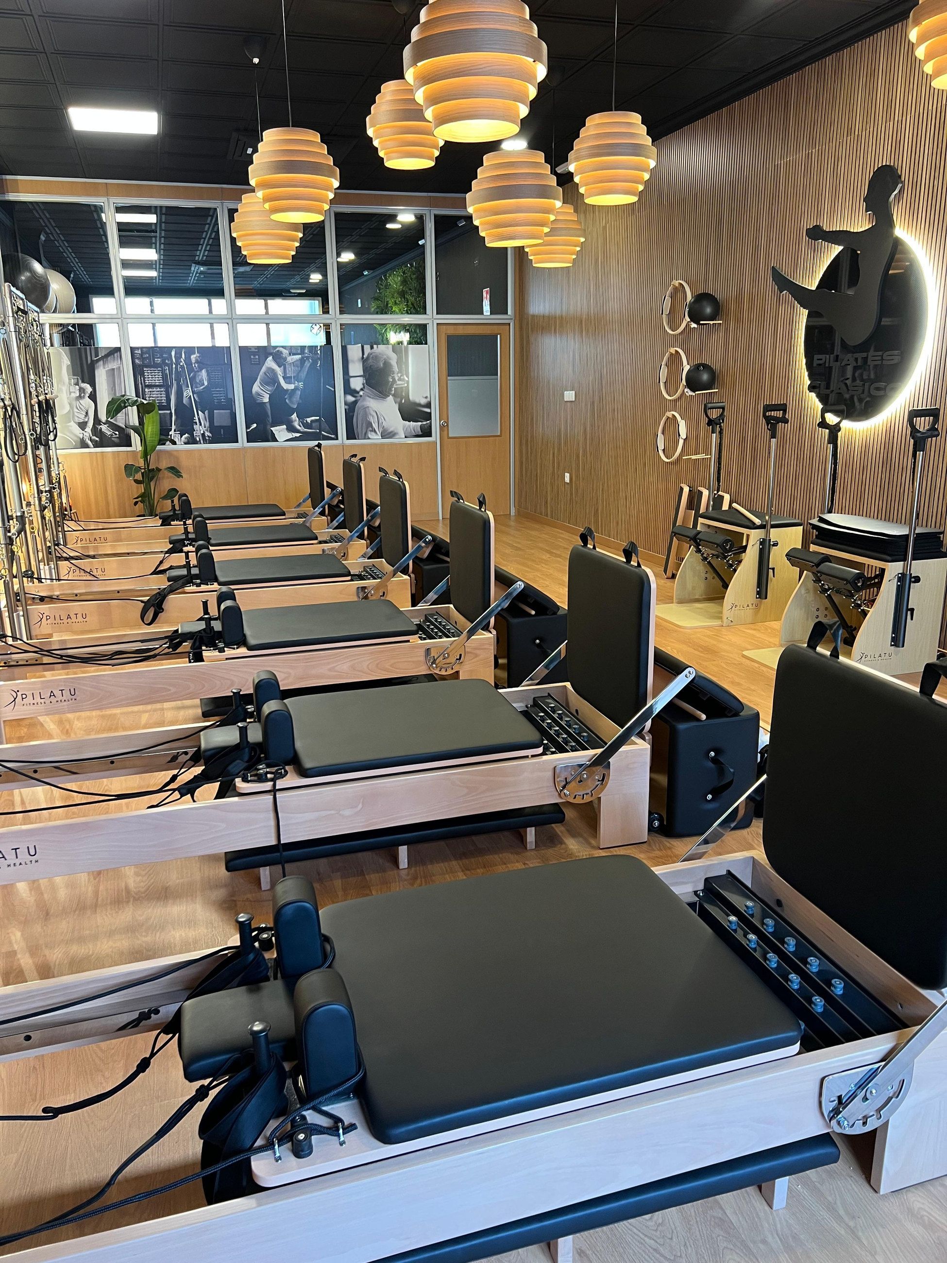 Fila de reformers de madera y cuero negro bajo lámparas cálidas en la sala de Pilates