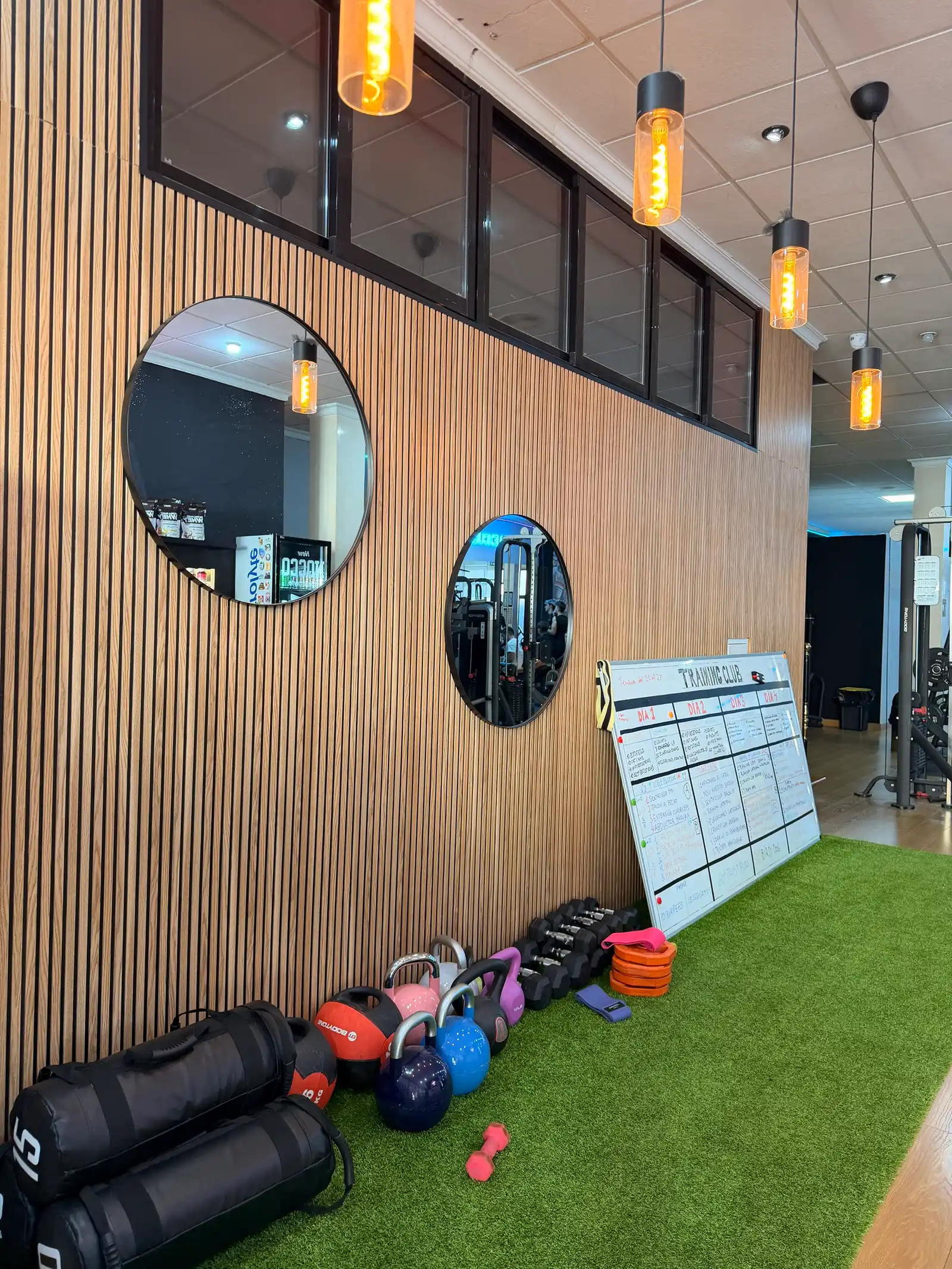 Pared de listones de madera con espejos redondos, lámparas y césped con kettlebells en la entrada de Hevy Fit